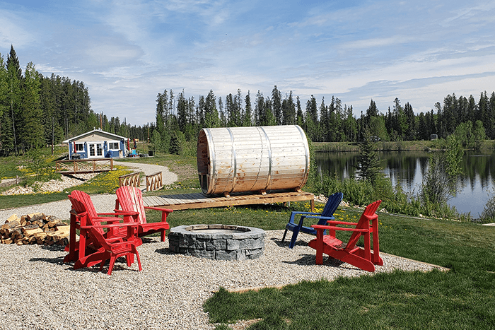 Red adirondak chairs around a firepit by a lake