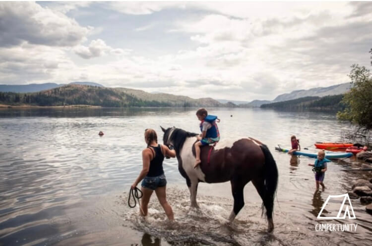 Child on horsebak by a lake with boats in foreground