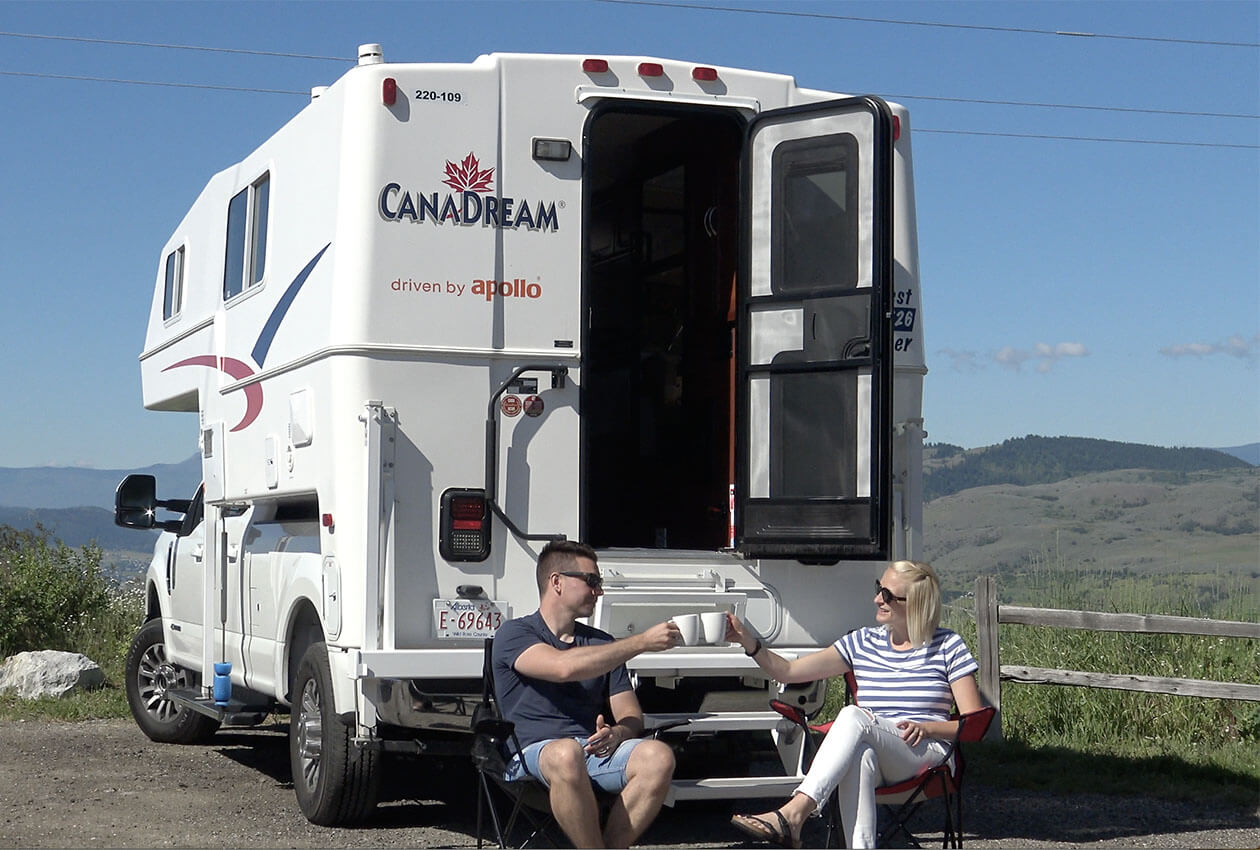 Couple sitting by CanaDream RV truck and camper drinking coffee