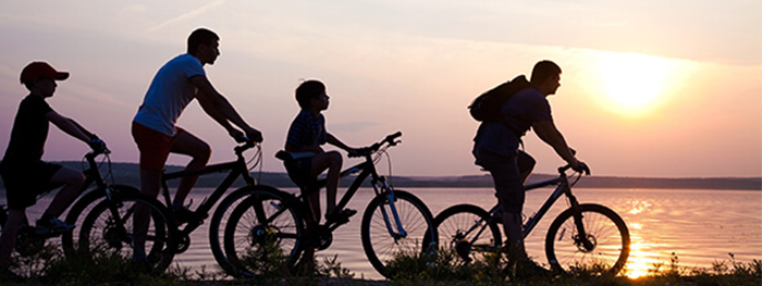 Family riding bikes next to a beach at sunset